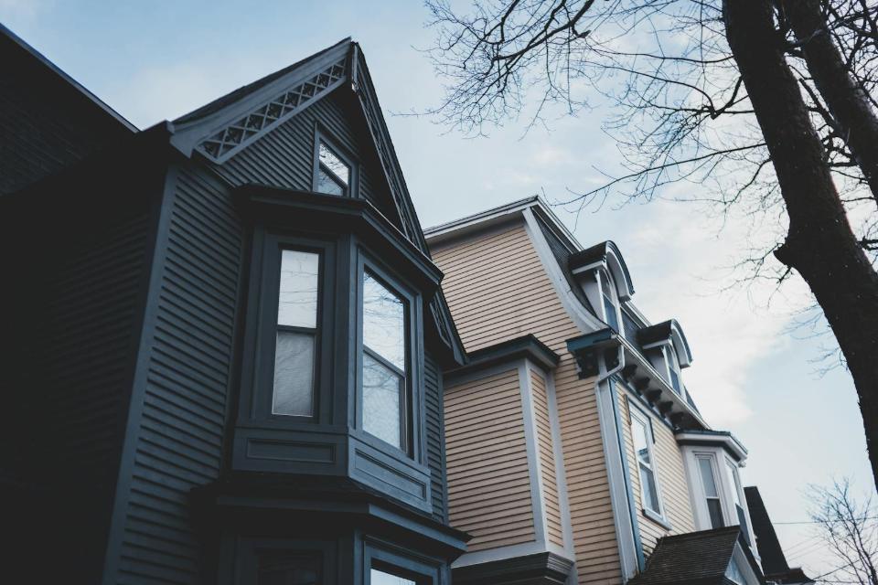 Upward view of two meticulously painted Victorian homes in San Francisco, showing dark and light siding, prominent bay windows, and architectural gables near the Mission District. This photograph provides an upward perspective of two striking, contrastingly painted Victorian residences common in the historic districts of San Francisco. The dark gray home features a dramatic gable and large bay window, standing beside a softer yellow structure with classic dormer windows. This juxtaposition perfectly illustrates the enduring architectural charm and detailing found in properties around the central neighborhoods of San Francisco.