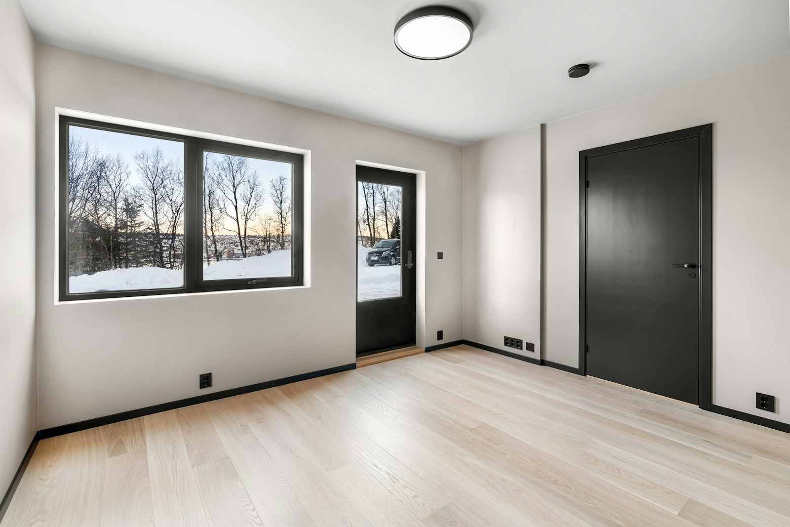Modern minimalist room design featuring light blonde engineered hardwood flooring, high-contrast black interior trim and doors, and large energy-efficient windows, showcasing premium renovation quality for San Francisco homes near Mission Dolores Park. This image highlights superior craftsmanship found in contemporary renovations across San Francisco. The space features sleek, light-colored engineered flooring complemented by bold black baseboards and modern doors, creating a striking contrast. Large, energy-efficient windows maximize natural light, reflecting the minimalist design ethos popular in high-end properties located near the Mission District.