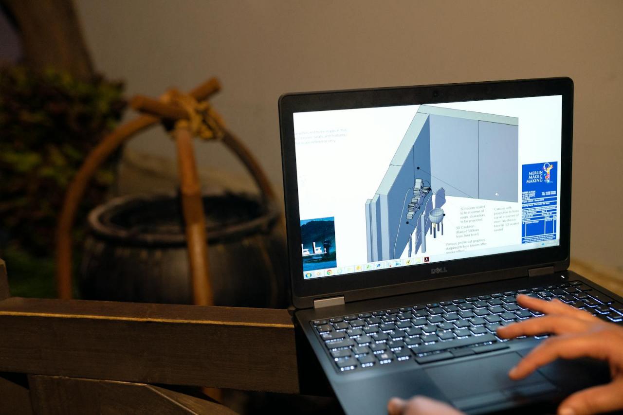 Close-up of a designer using a Dell laptop to review 3D CAD plans for a themed attraction installation, featuring the Merlin Magic Making logo, while working remotely from a casual, rustic setting in San Francisco, California. Modern engineering relies on seamless digital collaboration. Here, a design professional finalizes intricate 3D technical drawings on a Dell laptop. The displayed blueprints, including complex piping and structures marked with the Merlin Magic Making branding, demonstrate the level of detail required for large entertainment installations. This scene captures the flexibility of today's tech industry, allowing specialized design work to be executed remotely, connecting San Francisco's innovative talent pool with global projects.