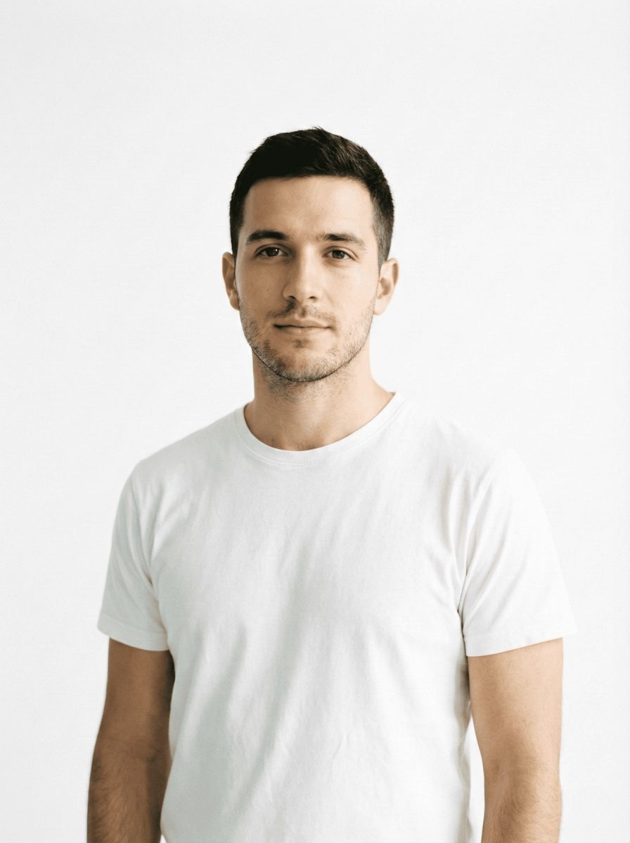 Professional portrait of a confident young male entrepreneur with short dark hair and a white t-shirt, ready for business in San Francisco's Mission District (37.767, -122.419). This high-quality, minimalistic portrait features a friendly young man, suitable for use on "About Us" pages, team profiles, or local business listings. His approachable demeanor reflects the welcoming spirit of local professionals serving the San Francisco area, particularly businesses located near the vibrant Mission District neighborhood.