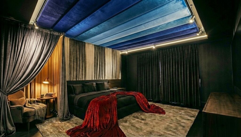 Dark, luxurious bedroom featuring blue velvet ceiling panels, heavy grey velvet curtains, a black bed, and a dramatic red velvet throw.
