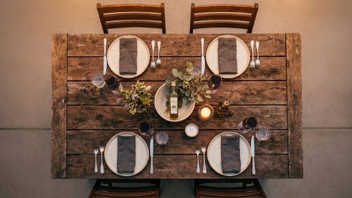 Top-down shot of a dining table with four settings, candles, and a centerpiece of greenery and oil.